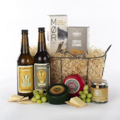 two bottles of cider, cheese, crackers, chutney in a wire basket