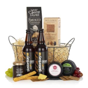 two bottles of cider, cheeses, crackers, and chutney presented in a wire basket