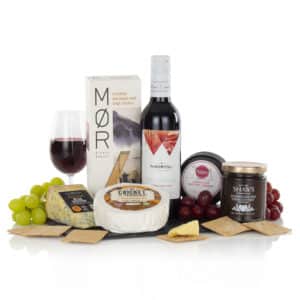 a bottle of red wine, three chesese, crackers, chutney, and a serving slate