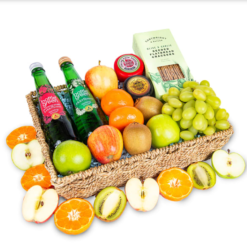 a basket with fruit, cheese, crackers, and two bottles of sparkling drink