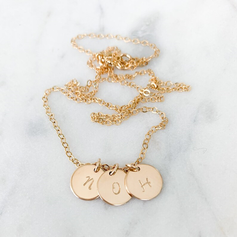 a gold necklace with three circle pendants and a letter on each