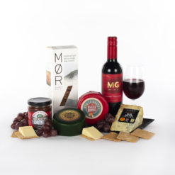 a bottle of red wine, three cheeses, chutney, and crackers on a slate